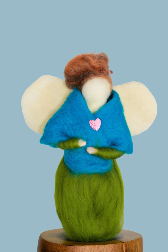 MariaElena | Handmade needle felted angel with auburn hair and teal blue cloak holding herself over a pink heart, cream wings spread, standing on green base – Guardian of Guidance comfort angel