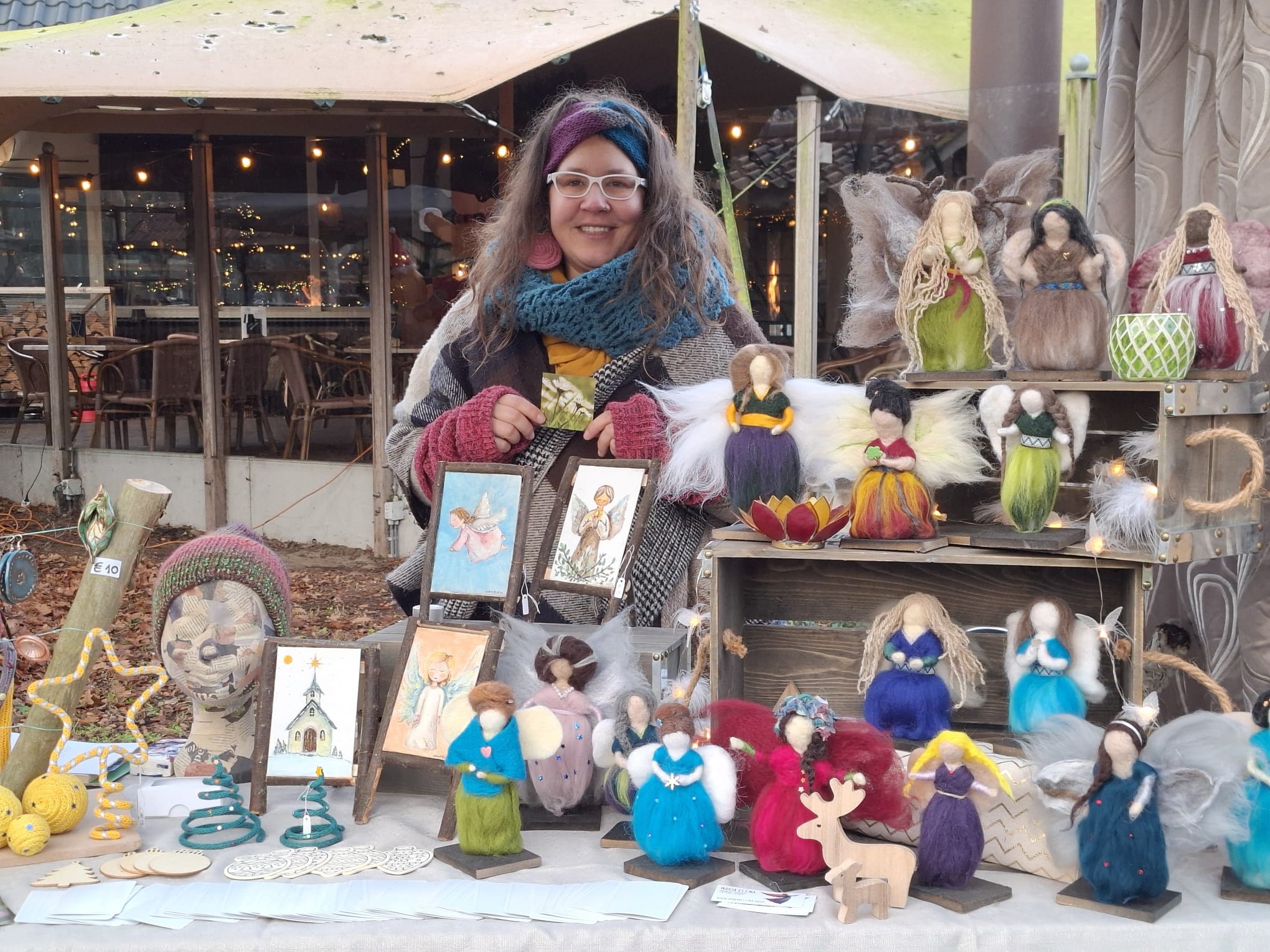 Artisan Maria at her Christmas market stall displaying colorful needle felted guardian angels, handmade ornaments, and therapeutic comfort angels in the Netherlands